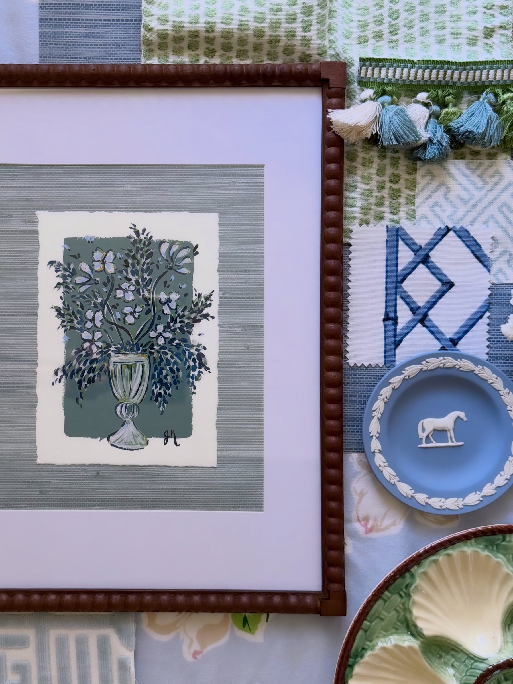 Framed artwork with floral design on a table with decorative plates and fabric.
